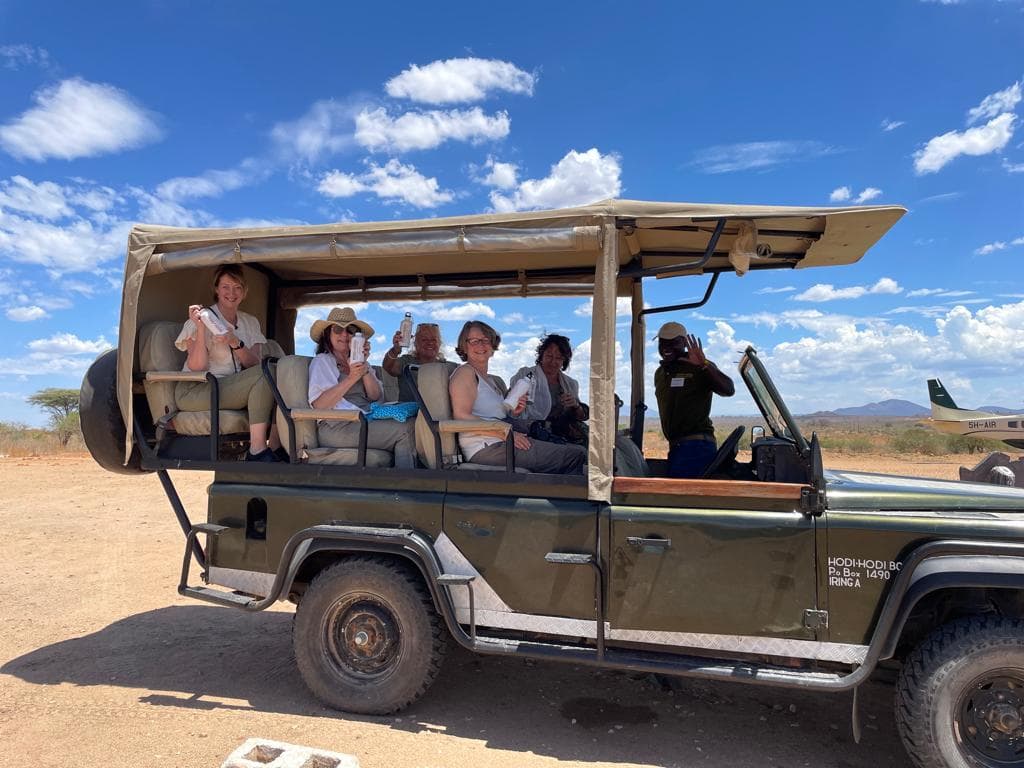 Guests in a safari vehicle beside a light aircraft at the airstrip